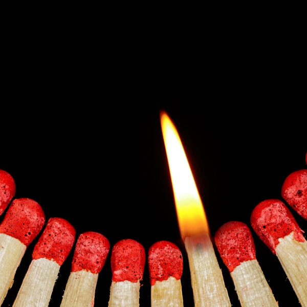 Zündhölzer mit einer brennenden Flamme in der Mitte, vor schwarzem Hintergrund angeordnet.