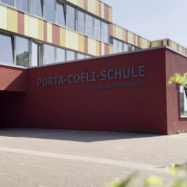 Eingang zur Porta-Coeli-Schule mit modernem Design und farbenfroher Fassade, umgeben von einem gepflegten Schulgelände.