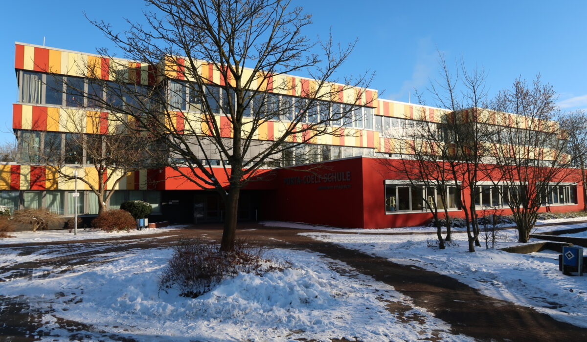 Moderne Schule Porta-Coeli mit farbenfroher Fassade, umgeben von Schnee und Bäumen, im Winterlicht.