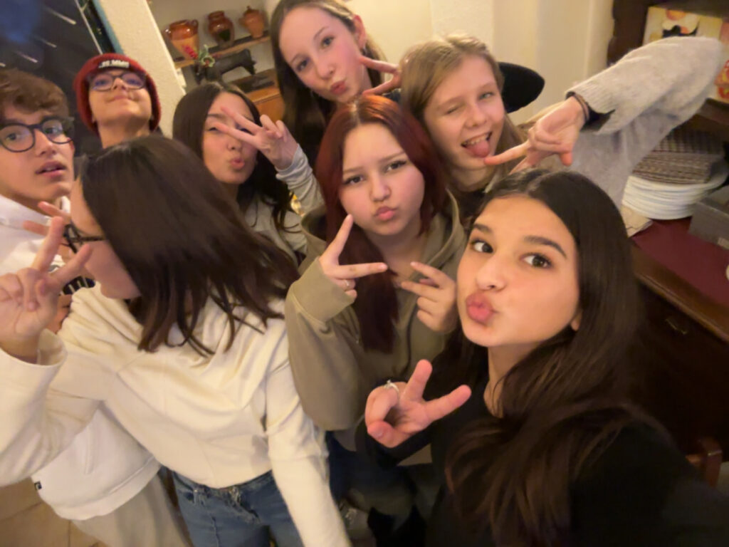 Gruppe von Jugendlichen, die Spaß haben und in die Kamera posieren, während sie Peace-Zeichen zeigen. Sie stehen in einem gemütlichen Raum mit dekorativen Elementen im Hintergrund.