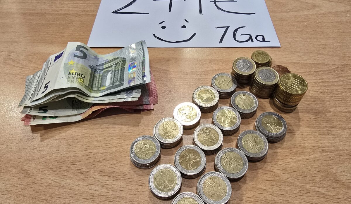 Stapel von Euro-Münzen und Scheinen auf einem Holztisch, mit einer Beschriftung von 241 € und einer Smileygrafik.
