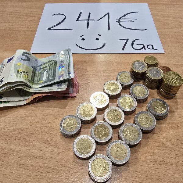 Stapel von Euro-Münzen und Scheinen auf einem Holztisch, mit einer Beschriftung von 241 € und einer Smileygrafik.