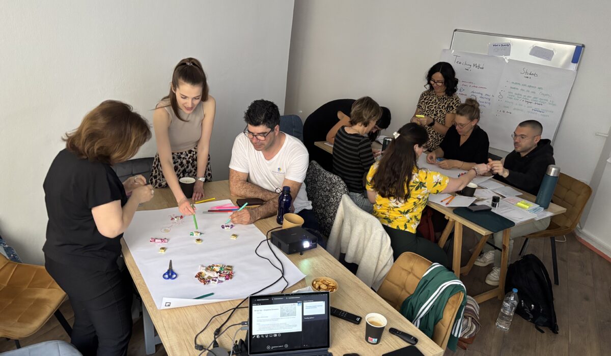 Gruppendiskussion in einem modernen Büro, bei der Teilnehmer an einem Tisch kreativ arbeiten. Auf dem Tisch liegen Bastelmaterialien, Notizen und ein Laptop. Die Atmosphäre ist kollaborativ und inspirierend.