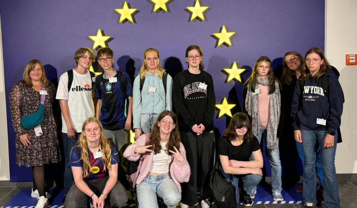 Gruppe von Jugendlichen und Betreuern vor einem Hintergrund mit goldenen Sternen, die die europäische Flagge symbolisieren, während einer Bildungs- oder Austauschveranstaltung.