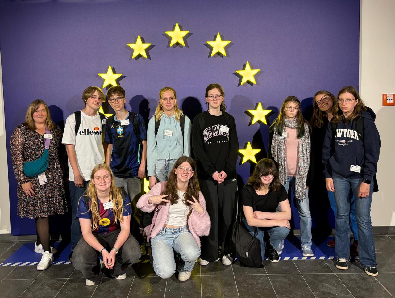 Gruppe von Jugendlichen und Betreuern vor einem Hintergrund mit goldenen Sternen, die die europäische Flagge symbolisieren, während einer Bildungs- oder Austauschveranstaltung.